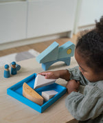 A child playing with the Grimm's blue boat Wooden Stacking Puzzle. The child is placing the blocks into the blue coloured wooden tray. These Grimm's toys are part of a wide range of wooden toys available here at Babipur. 