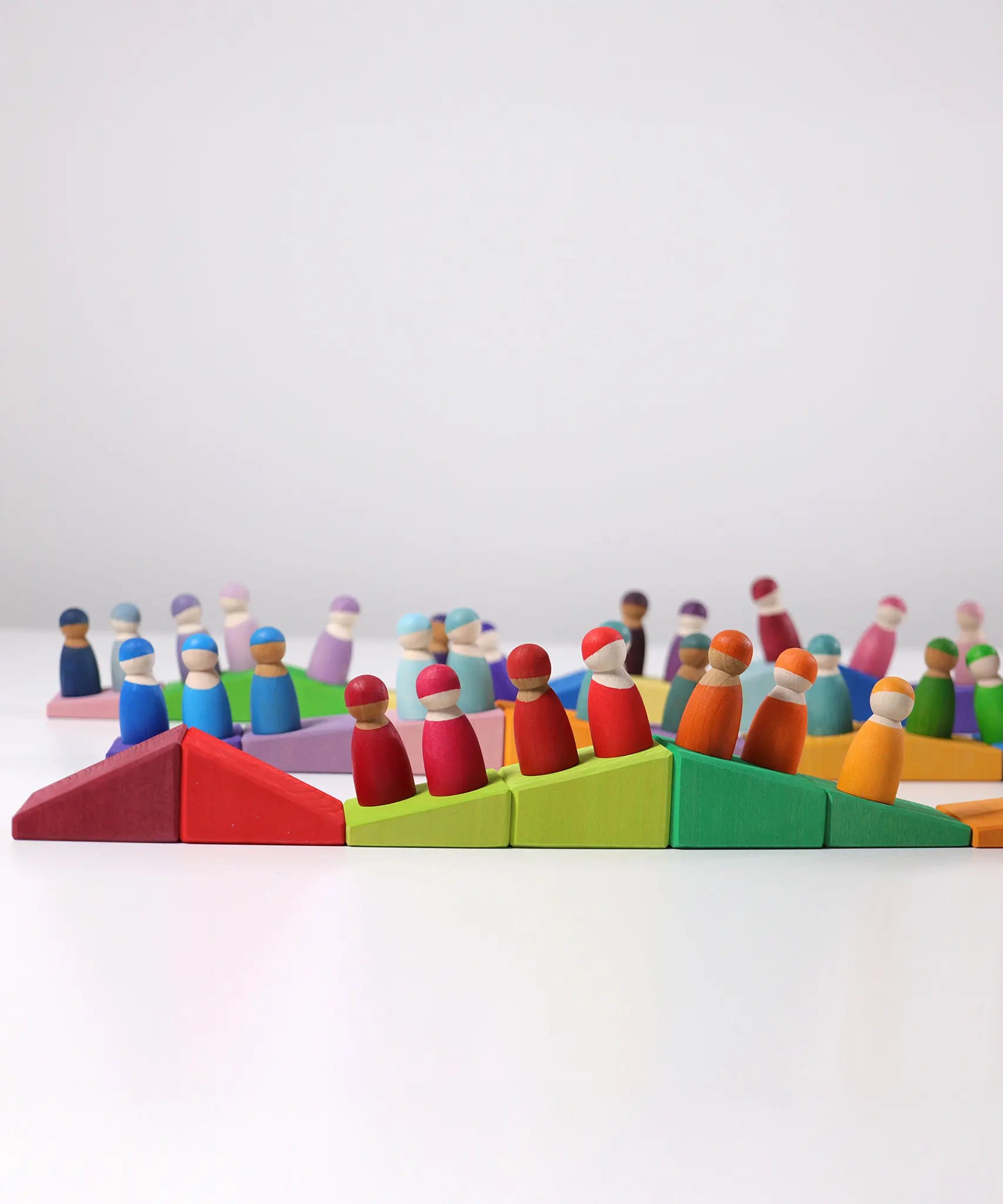 Grimm's sloping blocks building set blocks lined up with friends peg dolls placed on top of them.