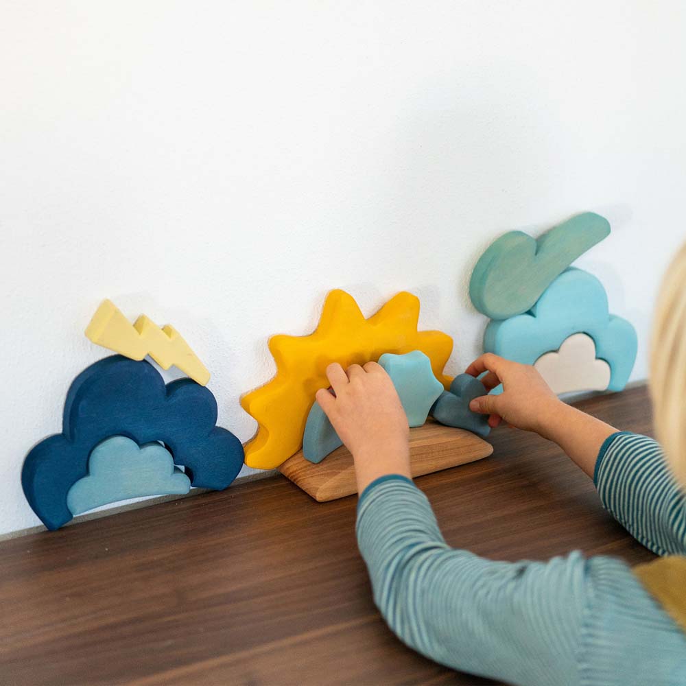 A child's hand arranging the pieces from the Grimm's weather set on a shelf. 