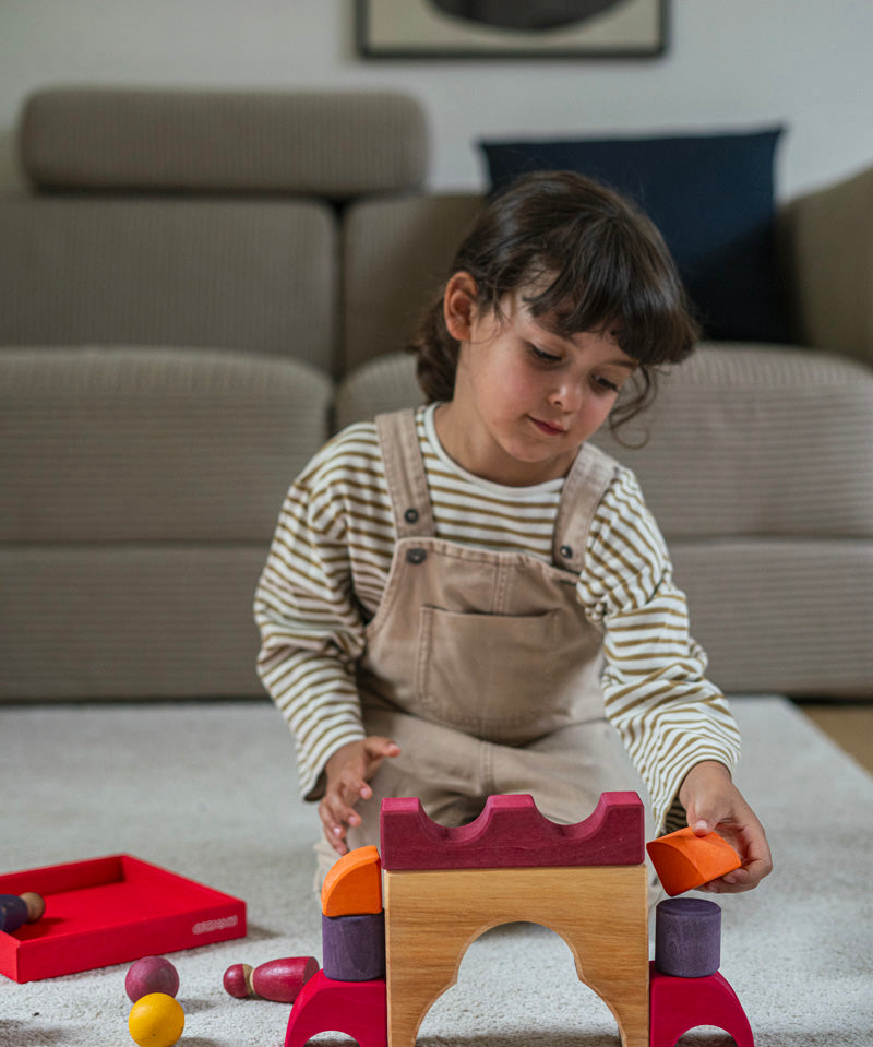 A child playing with the Grimm's red car stacking puzzle building block set. These Grimm's toys are part of a wide range of wooden toys available here at Babipur. 