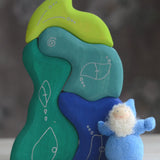 Grimm's handcrafted wooden casa aqua set with a small dwarf doll standing on top. Building blocks in shades of blue and green