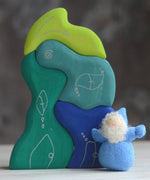 Grimm's handcrafted wooden casa aqua set with a small dwarf doll standing on top. Building blocks in shades of blue and green