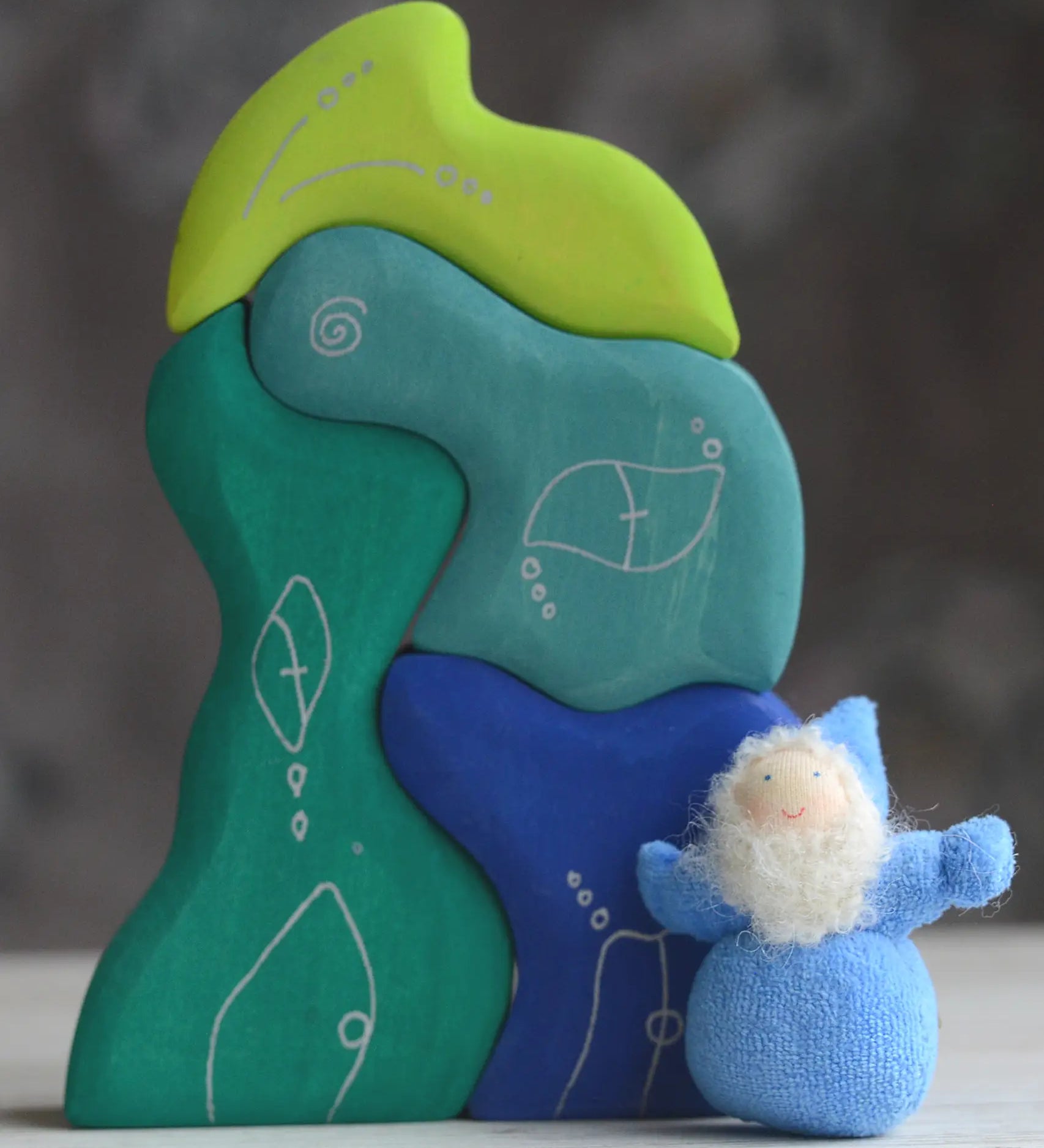 Grimm's handcrafted wooden casa aqua set with a small dwarf doll standing on top. Building blocks in shades of blue and green