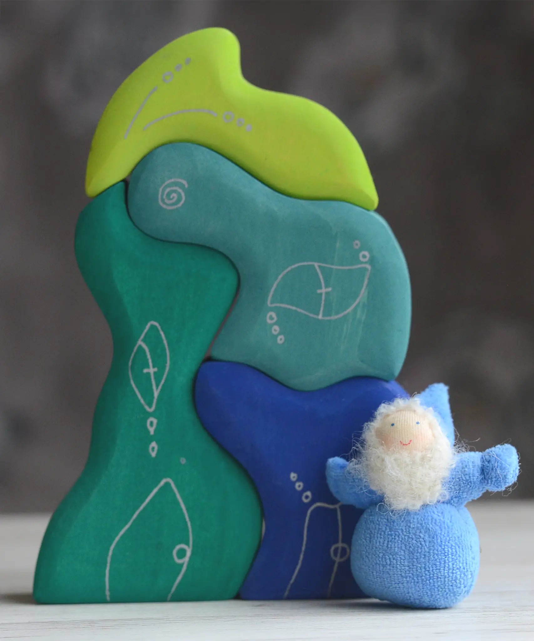 Grimm's handcrafted wooden casa aqua set with a small dwarf doll standing on top. Building blocks in shades of blue and green