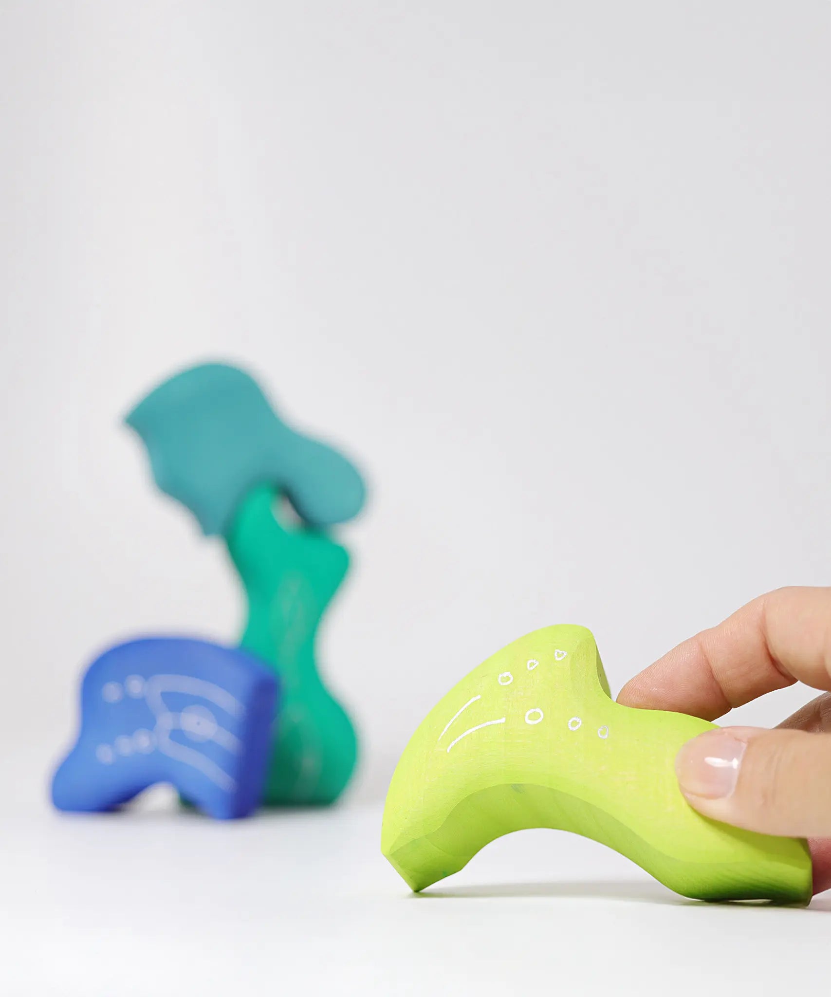 Adult holding a piece from the Grimm's casa aqua wooden toy stacking puzzle. Four piece simple wooden block puzzle toy in a mix of blue and green colours. 