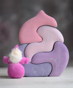 Grimm's handcrafted wooden casa coral set with a small dwarf doll standing on top. Building blocks in shades of purple