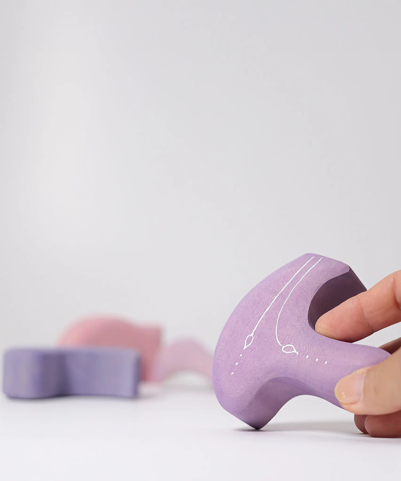 Adults holding a piece from the Grimm's casa coral wooden toy stacking puzzle. Four piece pink and lilac block puzzle. 
