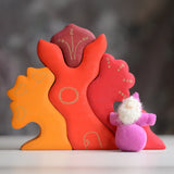 Grimm's handcrafted wooden casa glora set with a small dwarf doll standing on top. Building blocks in warm red and orange colours