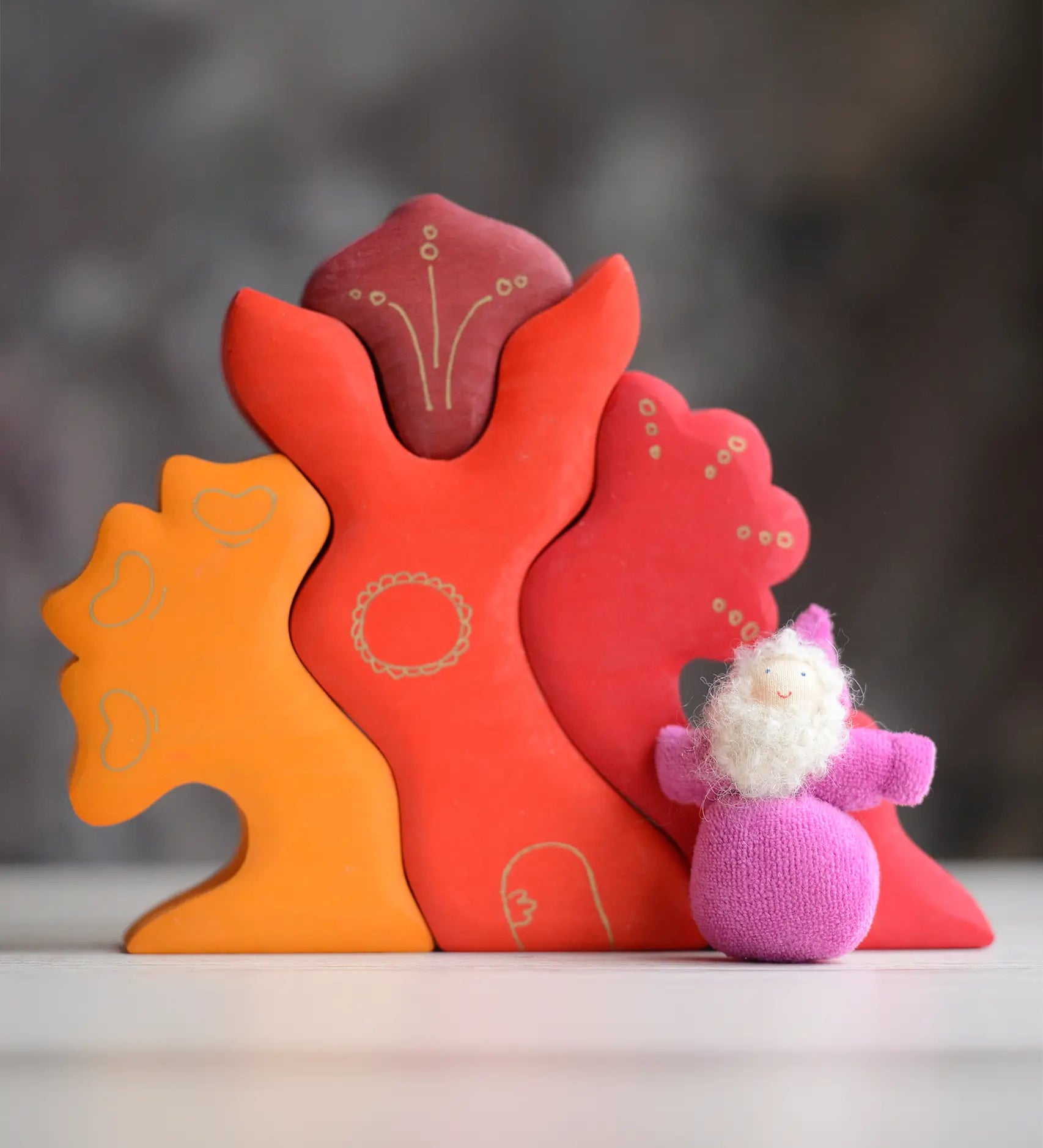 Grimm's handcrafted wooden casa glora set with a small dwarf doll standing on top. Building blocks in warm red and orange colours