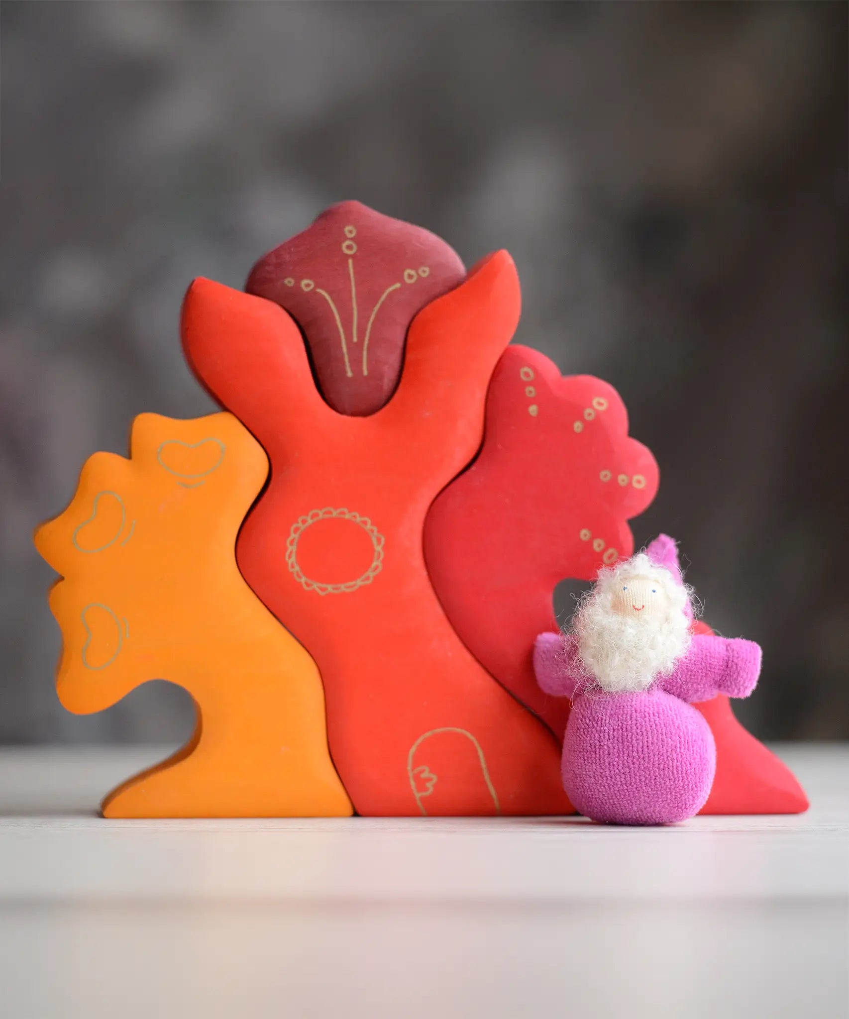 Grimm's handcrafted wooden casa glora set with a small dwarf doll standing on top. Building blocks in warm red and orange colours
