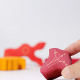 Adult's hand holding smallest piece from the Grimm's casa glora wooden toy stacking puzzle. 4 piece puzzle in a mix of red and yellow colours.