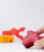 Adult's hand holding smallest piece from the Grimm's casa glora wooden toy stacking puzzle. 4 piece puzzle in a mix of red and yellow colours.