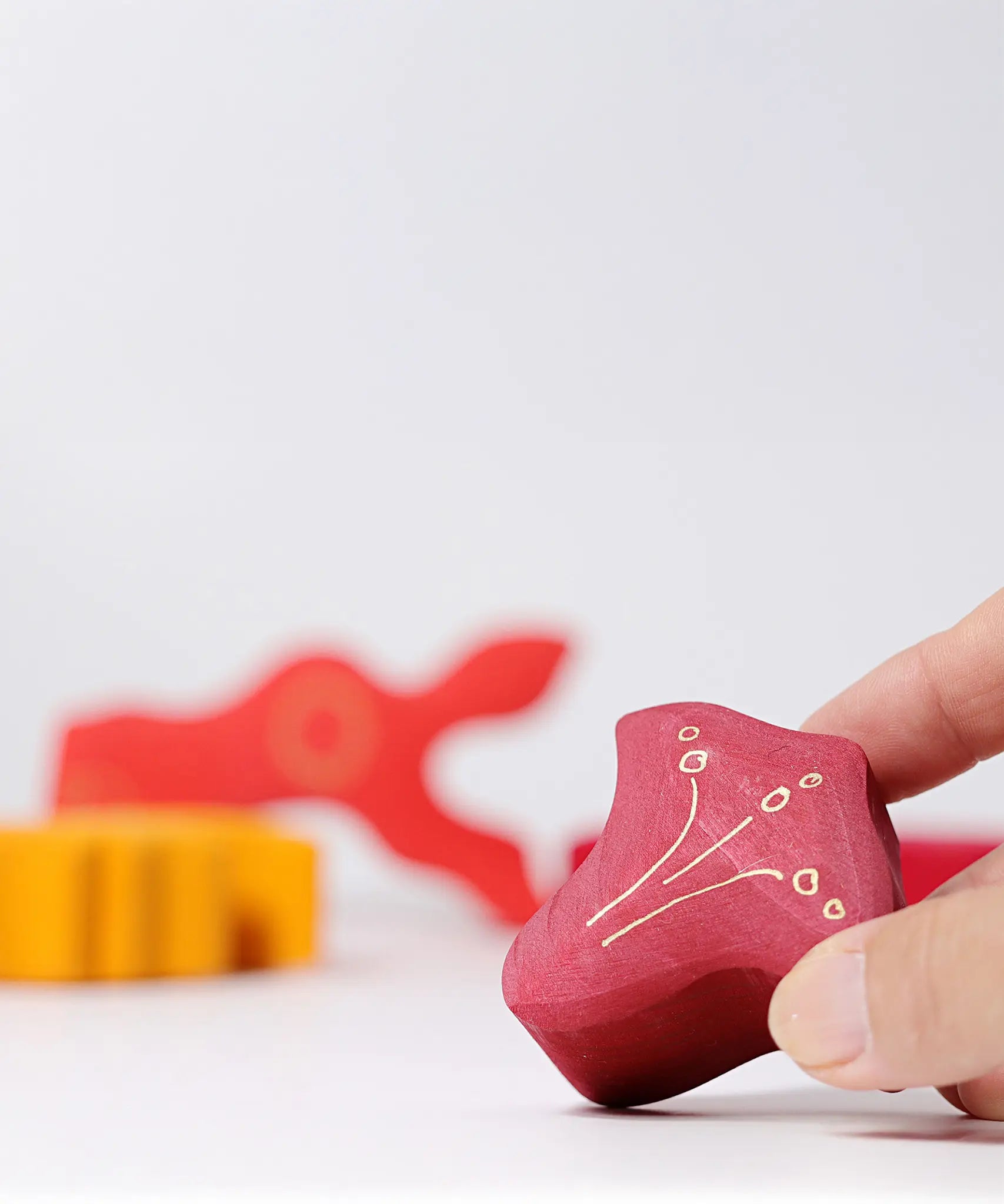Adult's hand holding smallest piece from the Grimm's casa glora wooden toy stacking puzzle. 4 piece puzzle in a mix of red and yellow colours.