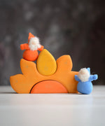 Grimm's handcrafted wooden casa sole set with small dwarf dolls standing on top. Building blocks in warm yellow and orange colours