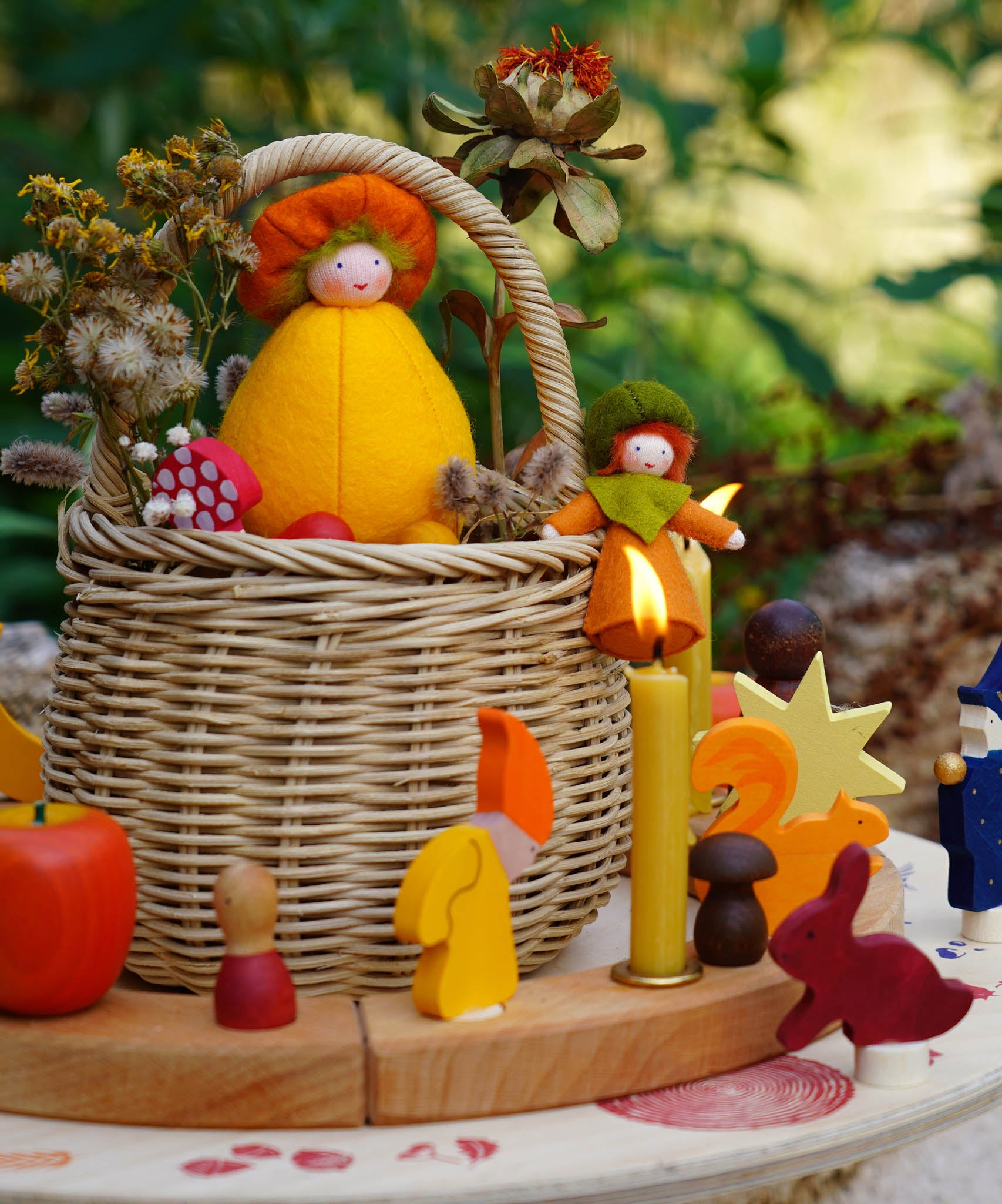 A cosy Autumn time display using a Grimm's Waldorf Celebration Ring, various Grimm's decorative figures and Grimm's Candles with a small basket in the middle holding various Ambrosius and Grimms figures available at Babipur.