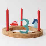 A Grimm's wooden celebration ring displaying  a red car, blue house, number 3 decoration figure and red candles