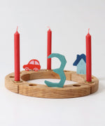 A Grimm's wooden celebration ring displaying  a red car, blue house, number 3 decoration figure and red candles
