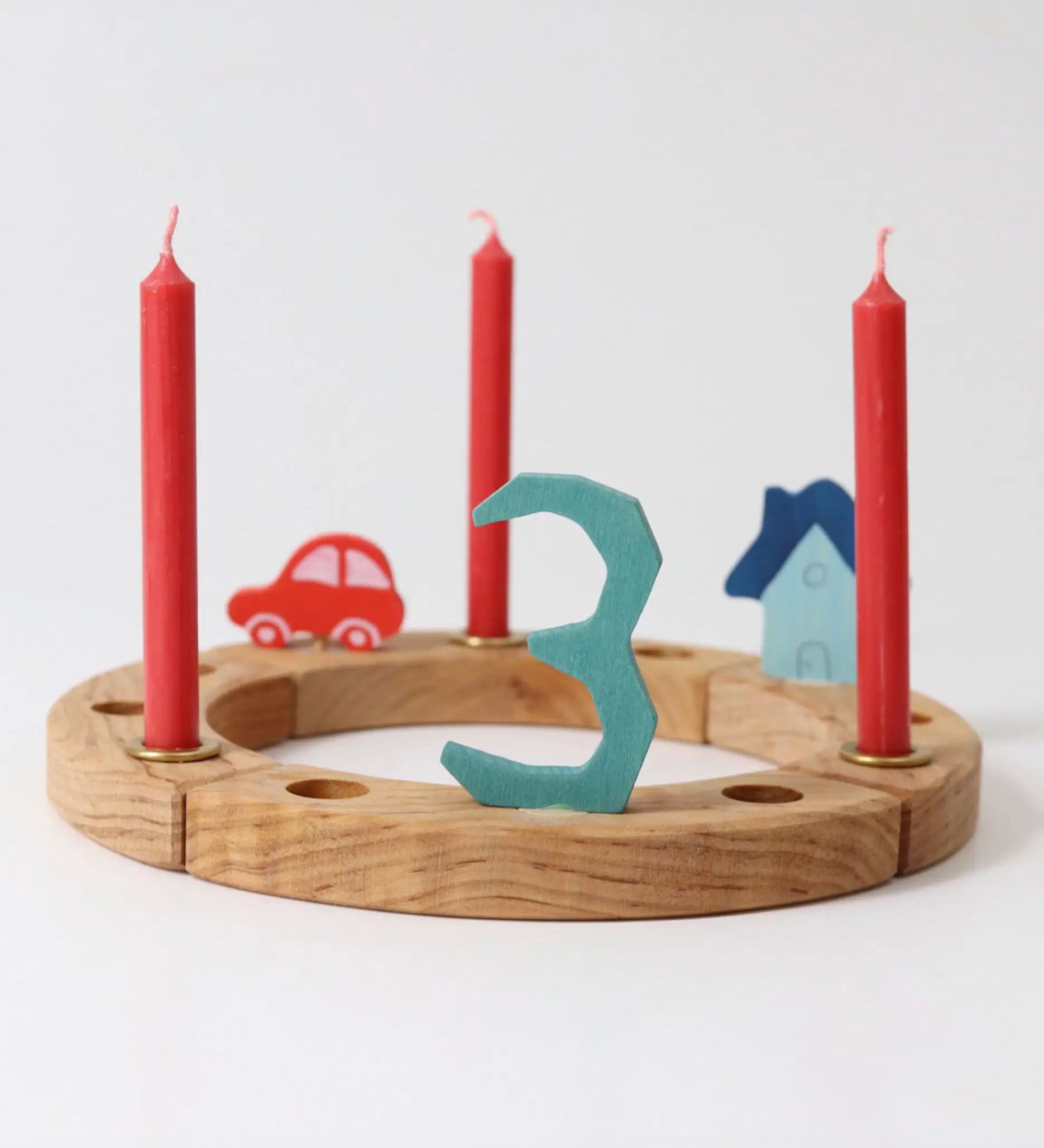 A Grimm's wooden celebration ring displaying  a red car, blue house, number 3 decoration figure and red candles