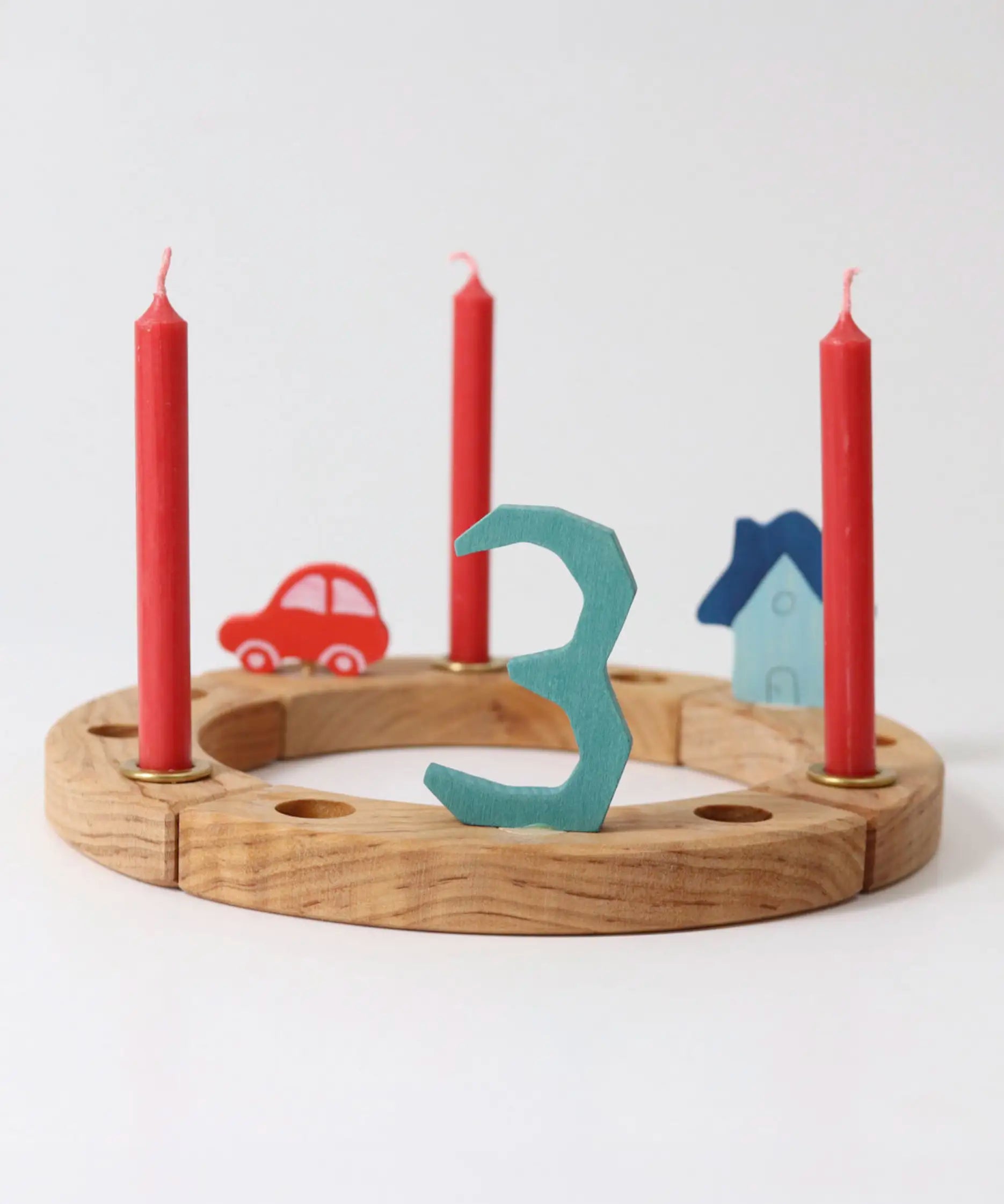 A Grimm's wooden celebration ring displaying  a red car, blue house, number 3 decoration figure and red candles
