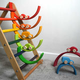 The cars from the Grimm's 6 Coloured Wooden Cars set placed on matching coloured pieces from the large Grimm's rainbow tunnel. Some pieces of the rainbow have been placed in the rungs of the Triclimb climbing frame. These wooden toy cars are part of a wide range of Grimm's wooden toys available here at Babipur.