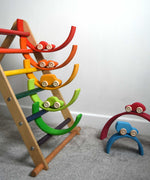 The cars from the Grimm's 6 Coloured Wooden Cars set placed on matching coloured pieces from the large Grimm's rainbow tunnel. Some pieces of the rainbow have been placed in the rungs of the Triclimb climbing frame. These wooden toy cars are part of a wide range of Grimm's wooden toys available here at Babipur.