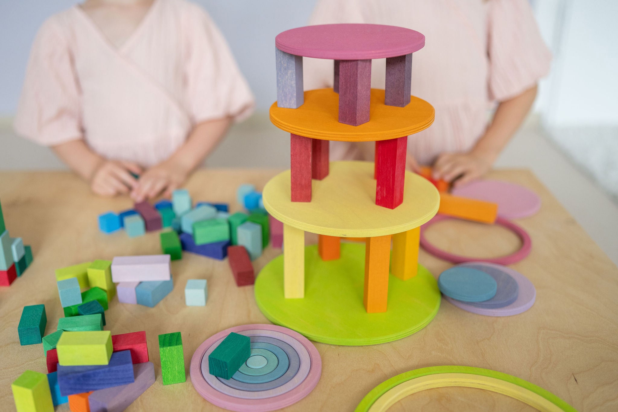 Two children playing with Grimm's wooden concentric circles and rings stacked into a colourful tower with wooden blocks, showcasing open-ended construction play.