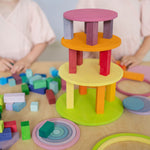 Two children playing with Grimm's wooden concentric circles and rings stacked into a colourful tower with wooden blocks, showcasing open-ended construction play.