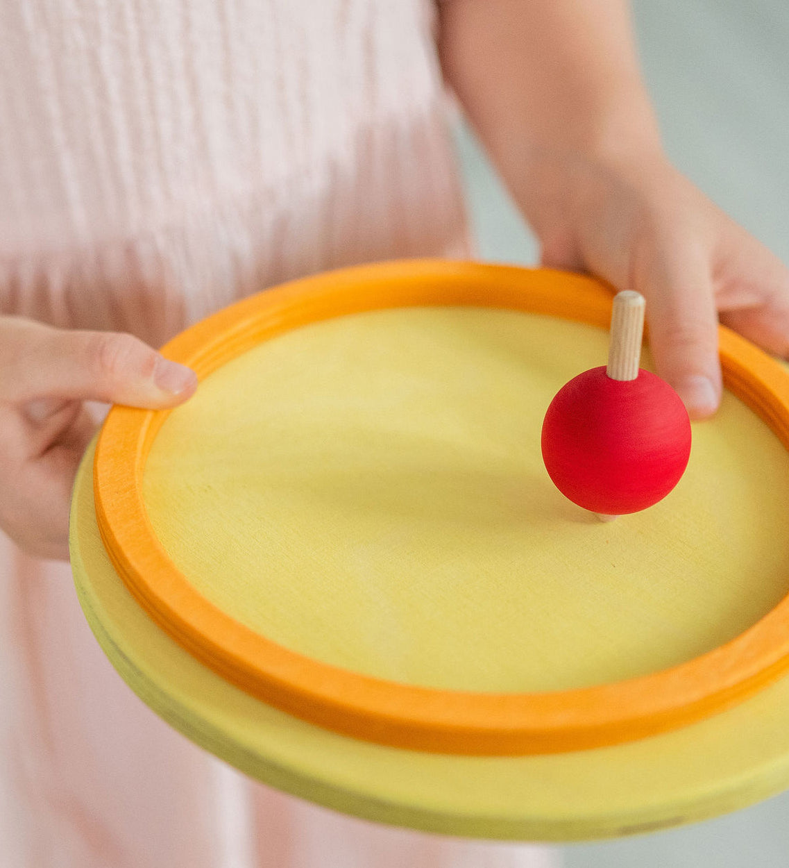 A little girl spinning a Grimm's wooden spinning top on one of the concentric circles