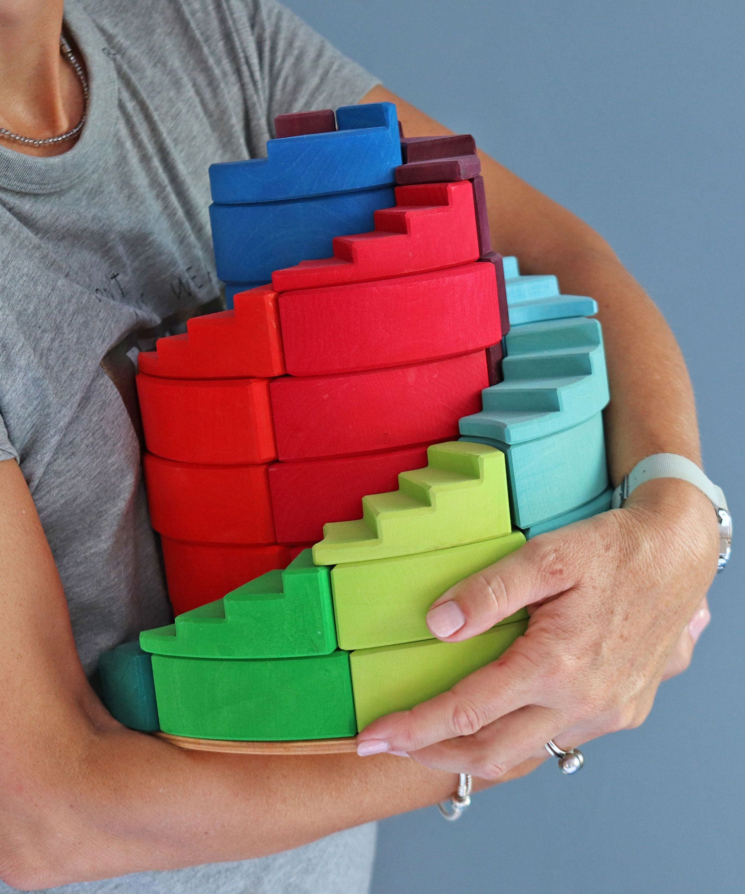 A person holding the Grimm's Counter-Rotating Stepped Spiral wooden block set in their arms.