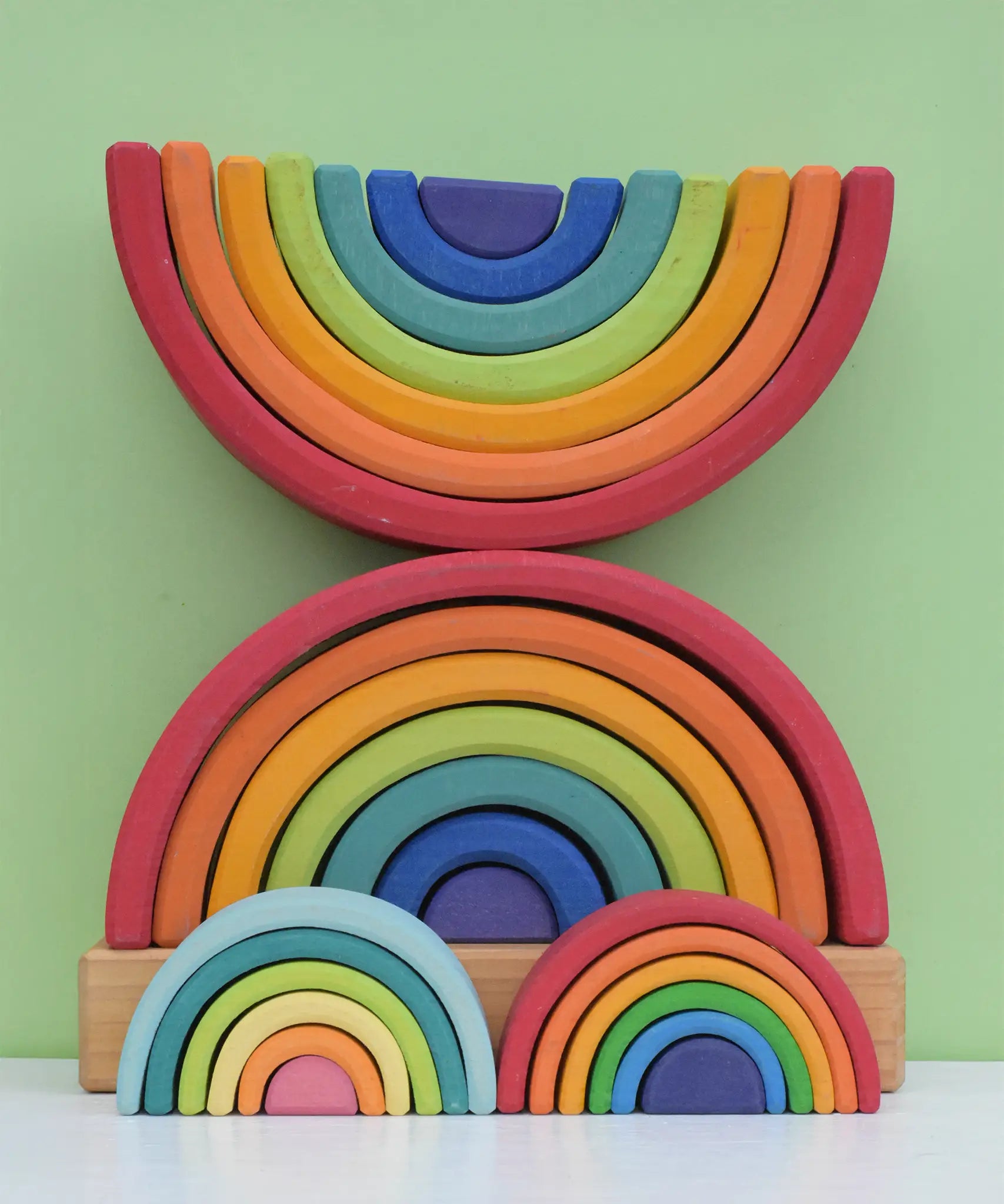 Grimm's Rainbow Stacking Tower with a rainbow and pastel mini rainbow placed in front of it. 