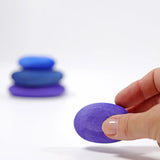Adult hand holding the smallest Grimms handcrafted wooden purple pebble piece showing scale