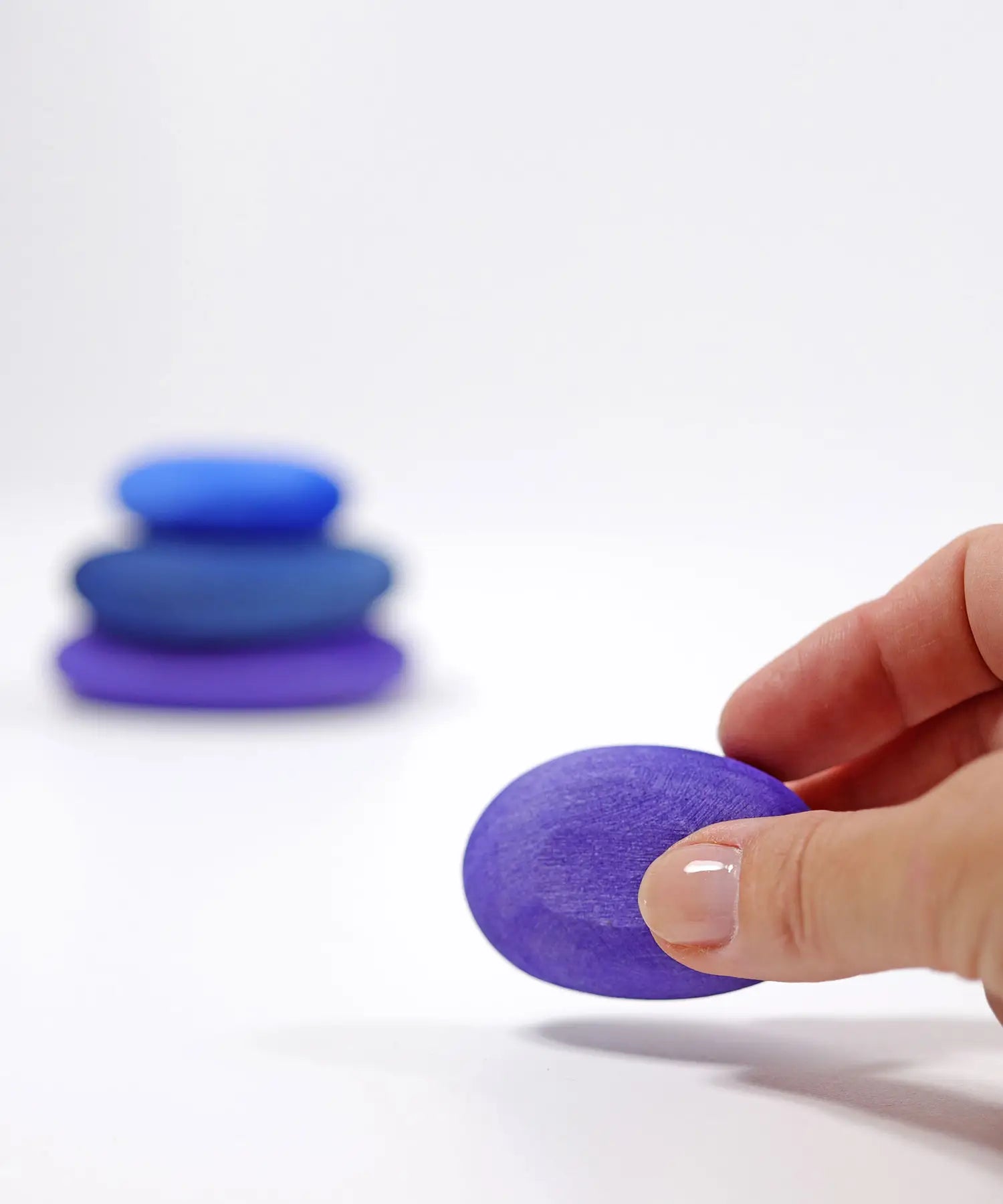 Adult hand holding the smallest Grimms handcrafted wooden purple pebble piece showing scale