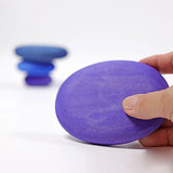 Adult hand holding the largest Grimms handcrafted wooden purple pebble piece showing scale