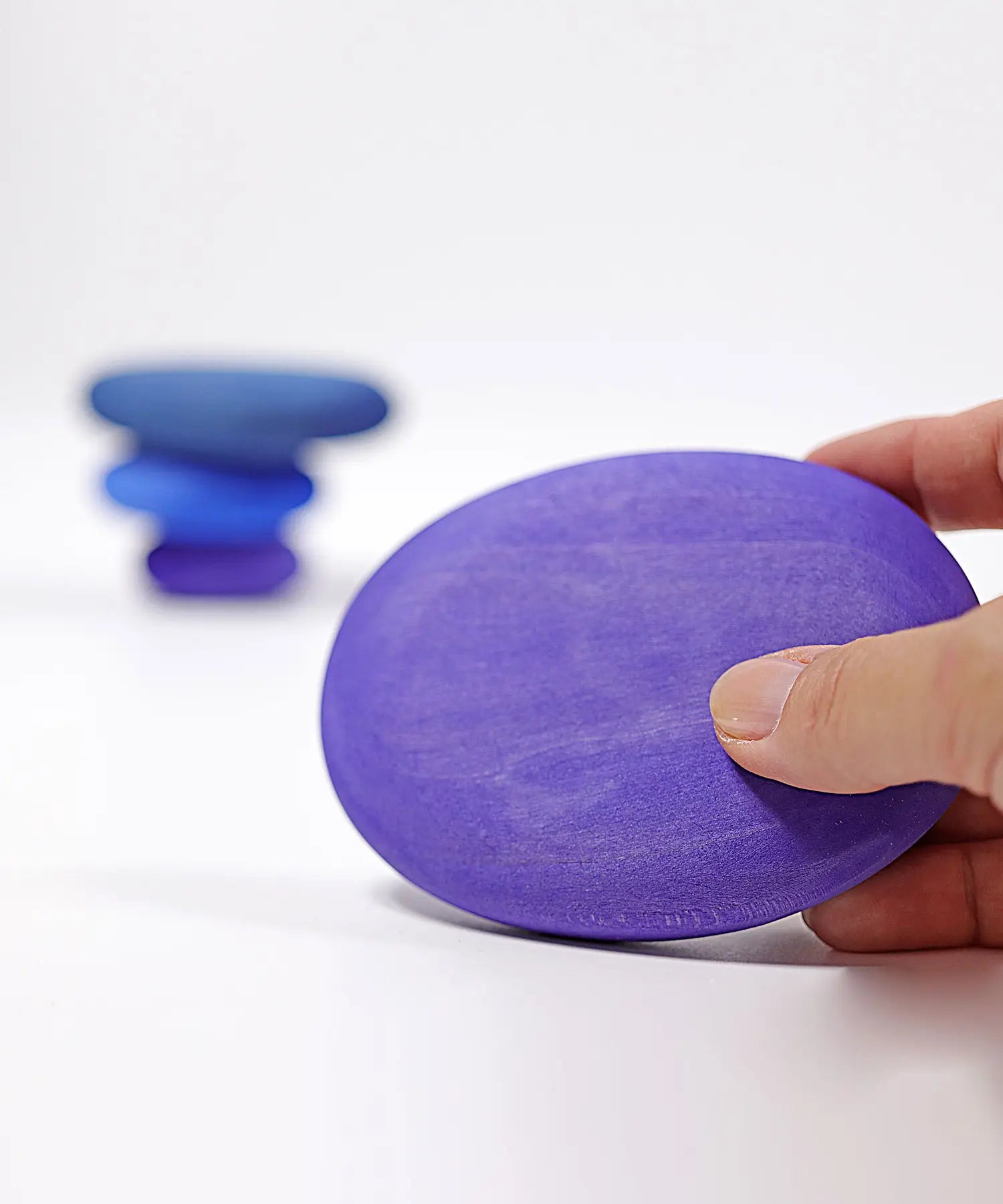 Adult hand holding the largest Grimms handcrafted wooden purple pebble piece showing scale