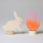 A Grimm's Easter Decorative Figure Set. the set includes a white bunny rabbit figure and a Batik Orange and purple coloured egg. 