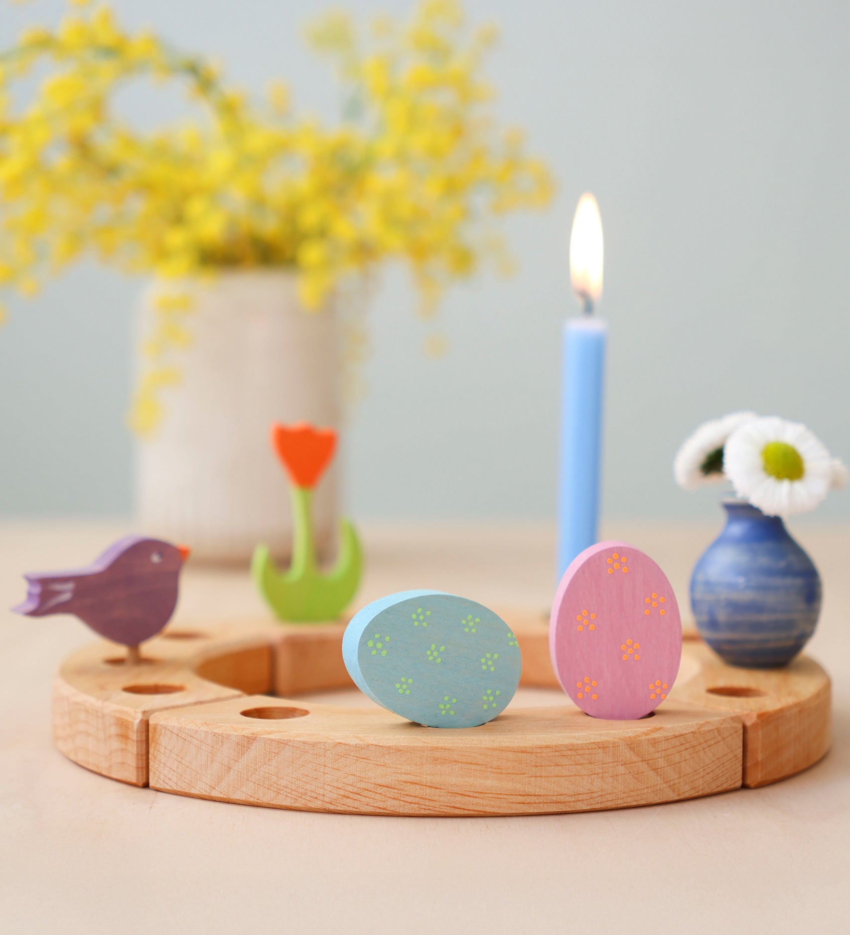 Grimm's pink and blue Floral Duo Easter Eggs Decorative Figure Set. Both eggs are placed on a wooden Grimm's celebration ring with other figures and a blue candle seen in the background.