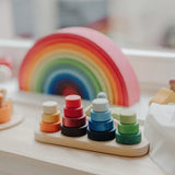 Grimms wooden fabuto stacking set standing next to a 12 piece rainbow arch  set