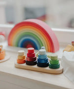 Grimms wooden fabuto stacking set standing next to a 12 piece rainbow arch  set