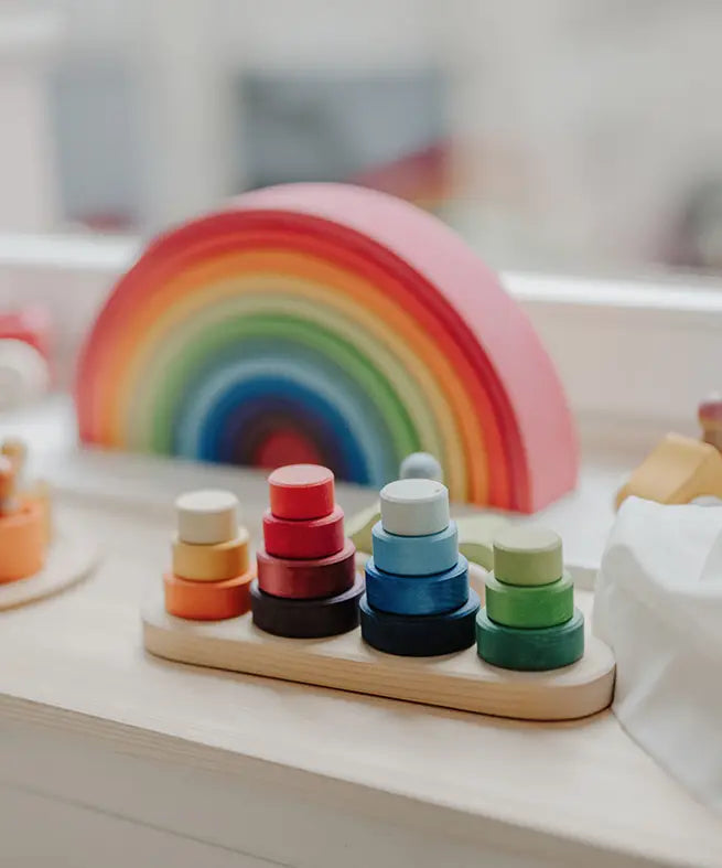 Grimms wooden fabuto stacking set standing next to a 12 piece rainbow arch  set