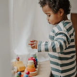 Child standing over a Grimms fabuto stacking set and holding a loose red disk