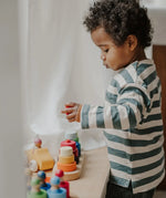 Child standing over a Grimms fabuto stacking set and holding a loose red disk