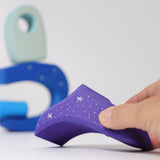 Adult hand holding a purple piece from the Grimms wooden fairytale village set showing the hand painted stars detail and scale