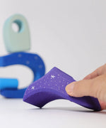 Adult hand holding a purple piece from the Grimms wooden fairytale village set showing the hand painted stars detail and scale