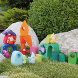 Pieces from the Grimm's fairytale village set loose on grass with dwarf dolls standing on top of the blocks