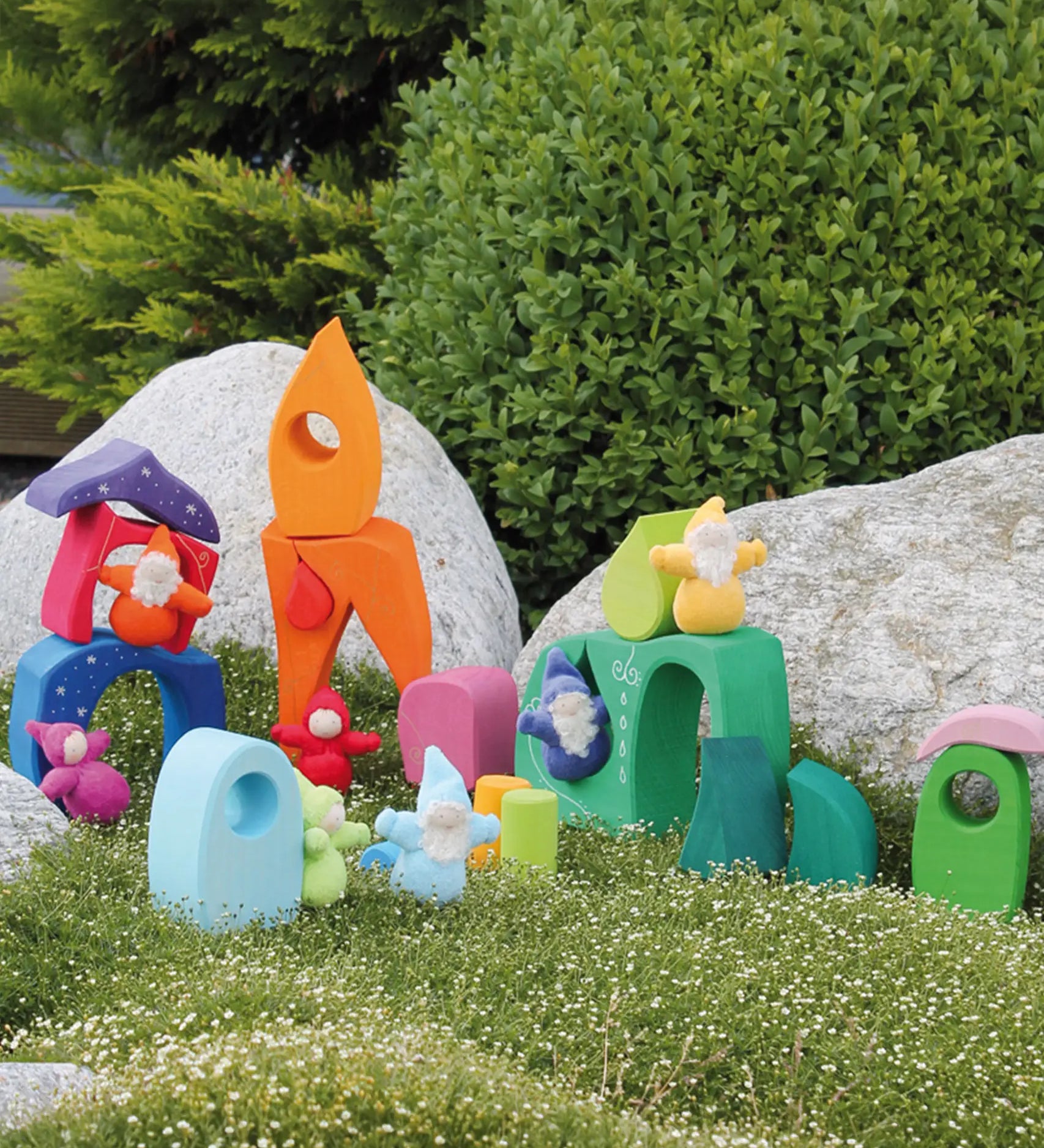 Pieces from the Grimm's fairytale village set loose on grass with dwarf dolls standing on top of the blocks