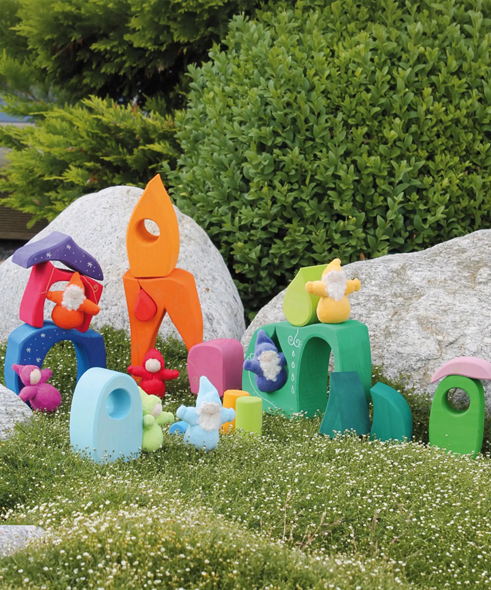 Pieces from the Grimm's fairytale village set loose on grass with dwarf dolls standing on top of the blocks