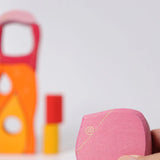 Adult hand holding a pink piece from the Grimms wooden fairytale village set showing scale