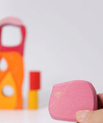 Adult hand holding a pink piece from the Grimms wooden fairytale village set showing scale