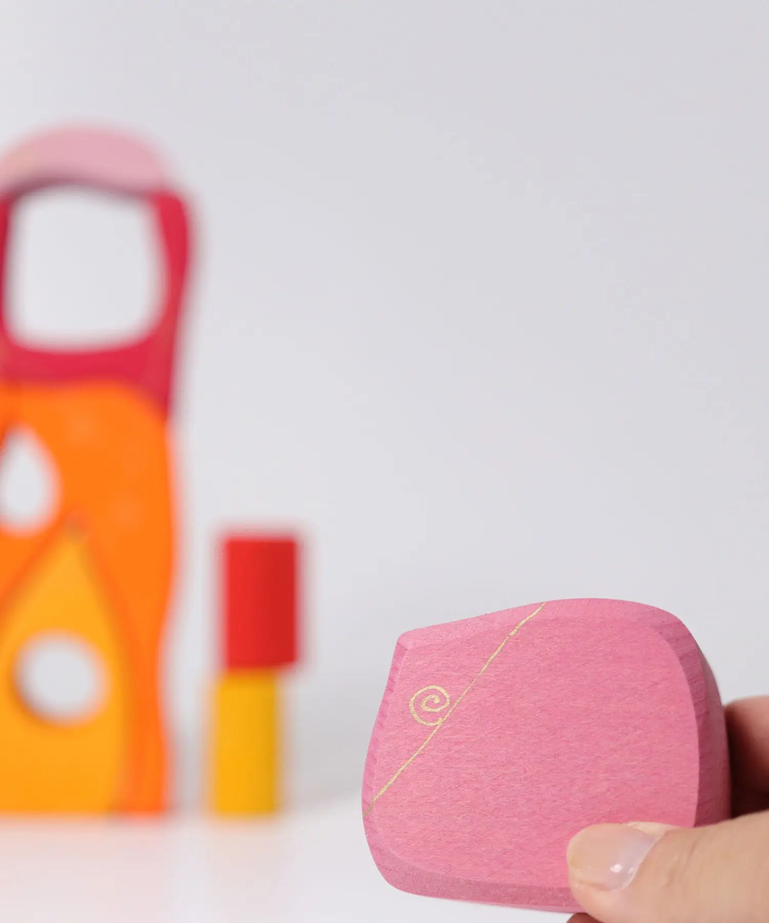 Adult hand holding a pink piece from the Grimms wooden fairytale village set showing scale