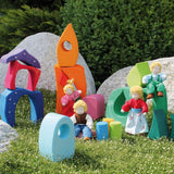 Pieces from the Grimm's fairytale village set loose on grass with waldorf dolls standing on top of the blocks